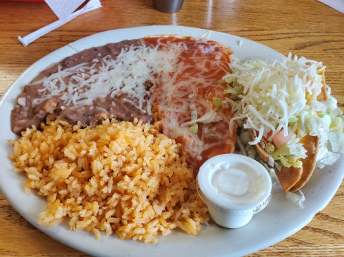 A plate of Mexican food featuring rice, refried beans, enchiladas with cheese, and a taco topped with lettuce and tomato.