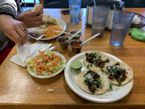 A table with two plates: tacos with meat and toppings, a salad with tomatoes and lettuce, and sauces in small bowls.