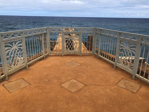 View from a seaside lookout with decorative railings and a path leading to the ocean. Cloudy sky above.