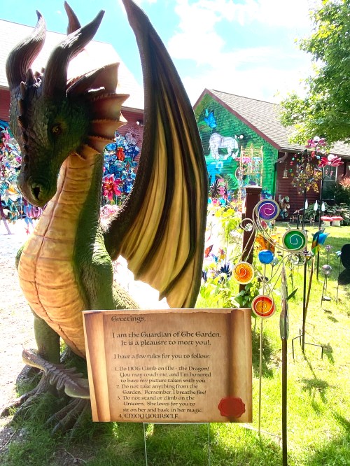 A colorful dragon statue stands in a garden, with a sign listing rules for visitors and whimsical decorations in the background.