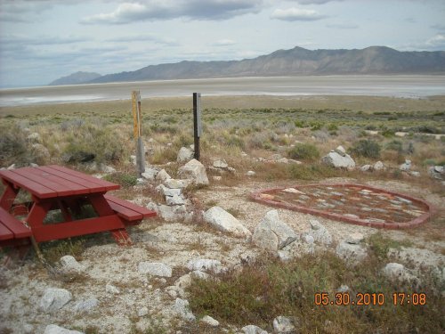 A red picnic table near a rocky area, overlooking a vast landscape with mountains in the distance and cloudy skies.