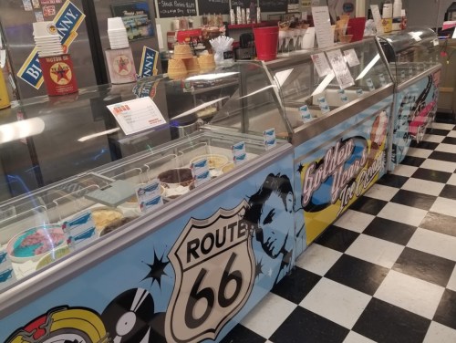 A colorful ice cream shop display featuring various ice cream flavors and Route 66 decor. Black and white checkered floor.