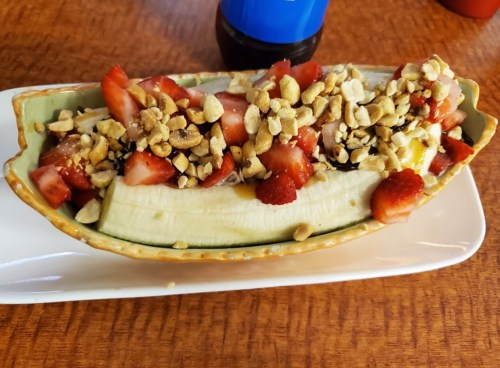 A banana split topped with strawberries, nuts, and drizzled with syrup, served in a decorative dish.