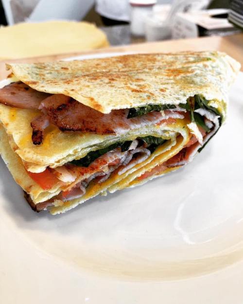 A layered sandwich with grilled chicken, ham, and vegetables, served on a plate.