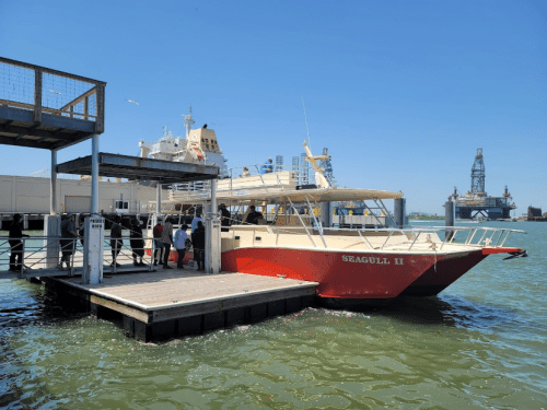 A red and white boat named "Seagull II" docked at a pier with people boarding, surrounded by water and industrial structures.