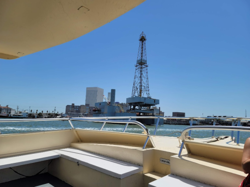 View from a boat showing a drilling rig and city skyline under a clear blue sky.
