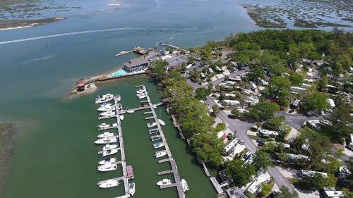 Aerial view of a marina with boats docked, surrounded by greenery and water, near a campsite.