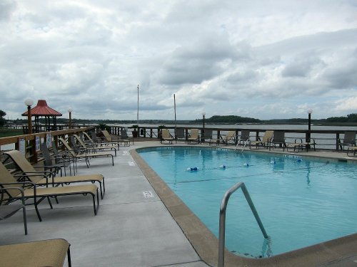 A serene pool area with lounge chairs, overlooking a calm lake under a cloudy sky.
