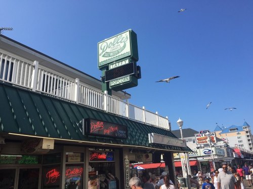 A busy boardwalk scene featuring a popcorn stand with a bright sign and seagulls flying overhead.