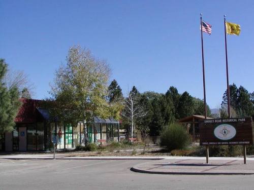 Smokey Bear Historical Park entrance with flags, trees, and a sign in a sunny outdoor setting.