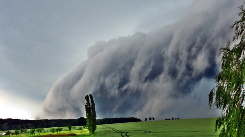 A dramatic cloud formation looms over a green field, creating a striking contrast against the darkening sky.