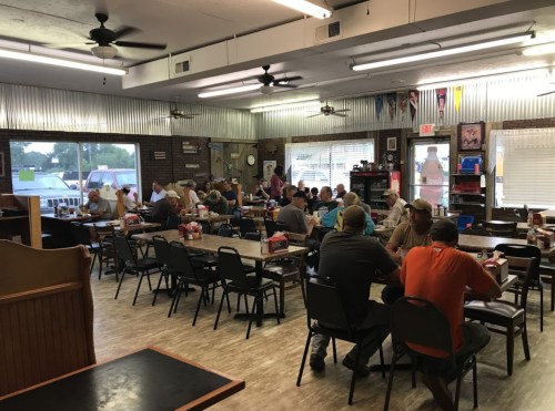 A busy diner with patrons seated at tables, enjoying meals in a casual, rustic setting.