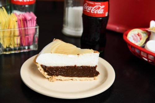 A slice of chocolate cream pie on a plate, with a bottle of Coca-Cola and condiments in the background.