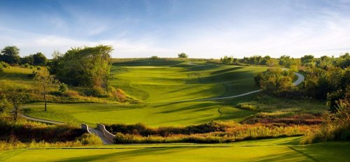 A scenic view of a lush green golf course with rolling hills and winding paths under a clear blue sky.