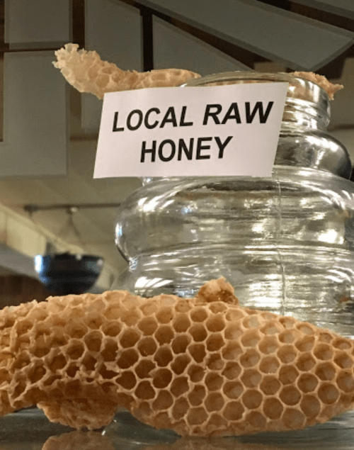 A jar of local raw honey with a piece of honeycomb beside it, displayed in a rustic setting.