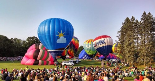 A vibrant scene of colorful hot air balloons at a festival, with a large crowd gathered on a grassy field.