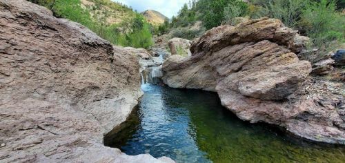 A serene rocky landscape featuring a small waterfall flowing into a clear pool surrounded by greenery.