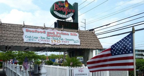 Sign for The Backfire Restaurant featuring a seafood and prime rib buffet, with an American flag in the foreground.