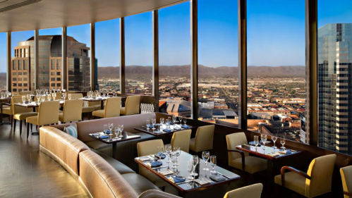 Elegant restaurant with panoramic city views, featuring stylish seating and tables set for dining.