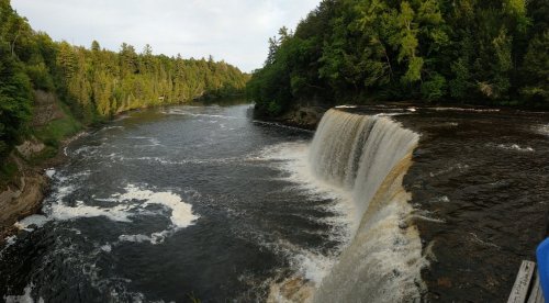 A scenic view of a waterfall cascading into a river, surrounded by lush green trees and a serene landscape.