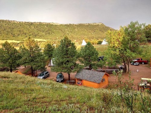 A scenic view of a campsite with cabins, tents, and vehicles surrounded by trees and hills.