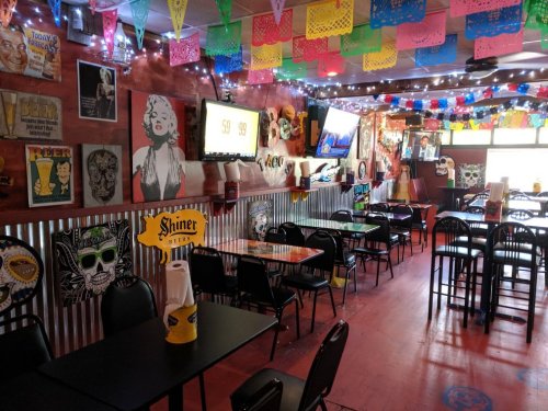 Colorful restaurant interior with festive decorations, tables, and wall art featuring various pop culture icons.