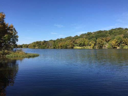A serene lake surrounded by lush trees under a clear blue sky, reflecting the vibrant colors of autumn.