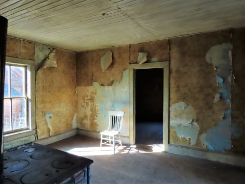 A sunlit room with peeling wallpaper, featuring a single white chair and an open door.