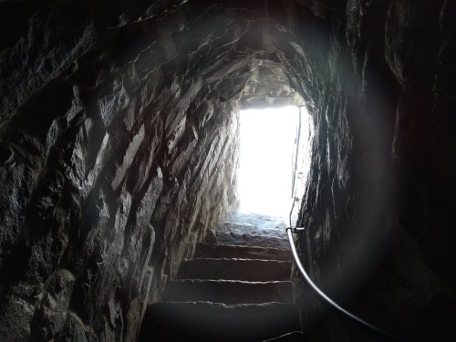 A dimly lit stone staircase leading upward, with a bright light visible at the top.