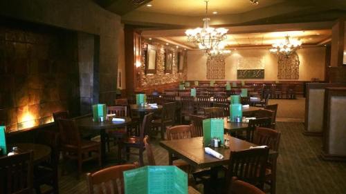 Interior of a restaurant featuring wooden tables, green menus, and a stone wall with a fireplace.