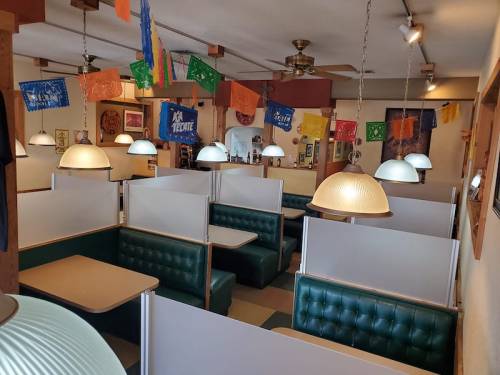 Interior of a cozy restaurant featuring green booths, pendant lights, and colorful banners hanging from the ceiling.