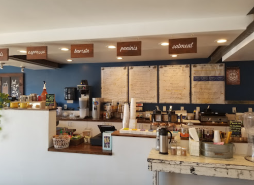Cozy café interior featuring a counter with menu boards, coffee machines, and a variety of food items displayed.