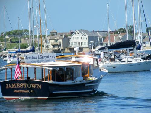 A ferry boat labeled "Jamestown & Newport Ferry" navigates a harbor filled with sailboats and waterfront homes.
