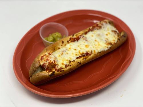 A cheesy hot dog on a red plate, topped with marinara sauce, served with a side of pickles.