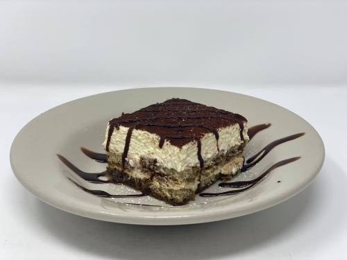 A slice of tiramisu on a beige plate, drizzled with chocolate sauce and dusted with powdered sugar.