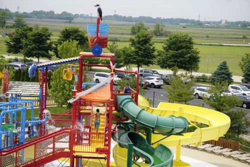 A colorful water park with slides, a climbing structure, and people enjoying the attractions on a sunny day.