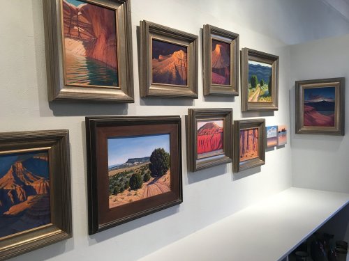 A gallery wall featuring several framed landscape paintings in warm colors, showcasing natural scenery.