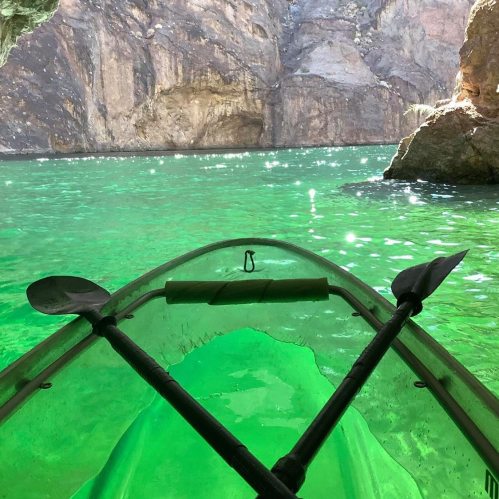 A kayak on vibrant green water, surrounded by rocky cliffs and sunlight filtering through.
