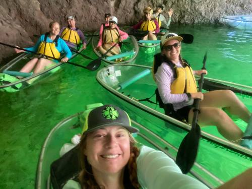 A group of seven people kayaking in a cave with green water, smiling and enjoying their adventure.