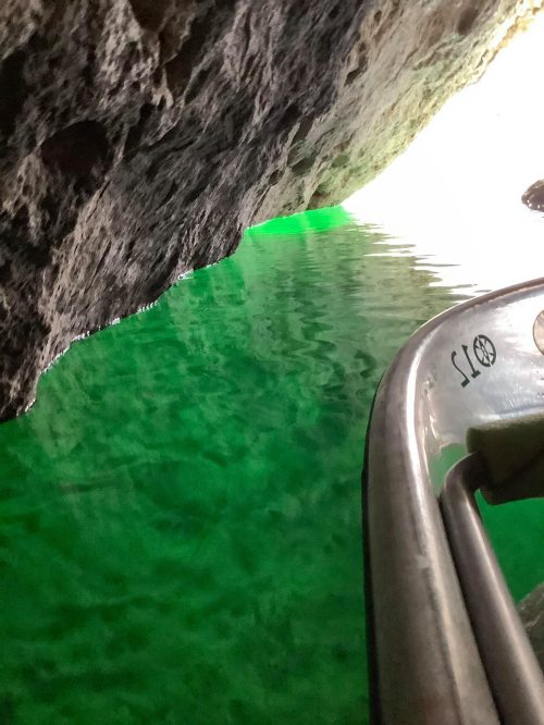 A view from a boat showing green water reflecting light, with rocky cave walls on either side.