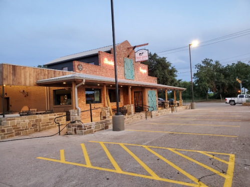 A rustic restaurant exterior with wooden accents, outdoor seating, and a sign, set against a twilight sky.