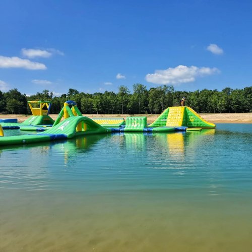 A colorful inflatable water park with slides and obstacles on a lake, surrounded by trees and a clear blue sky.