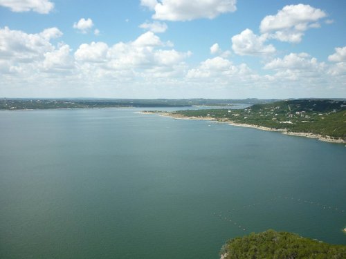 A scenic view of a calm lake surrounded by green hills and a blue sky with fluffy clouds.