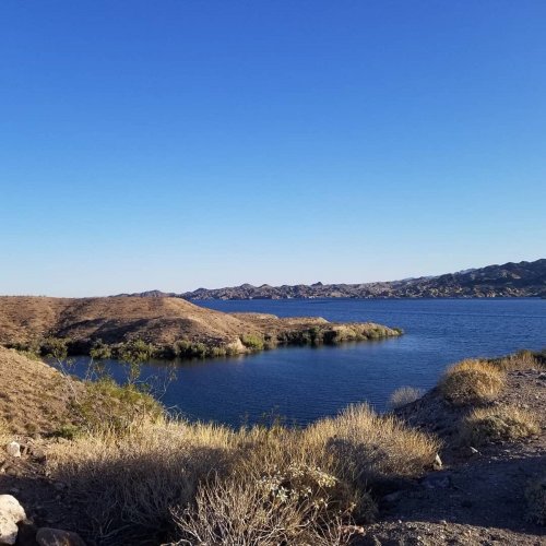 A serene landscape featuring a calm lake surrounded by dry hills and clear blue skies.