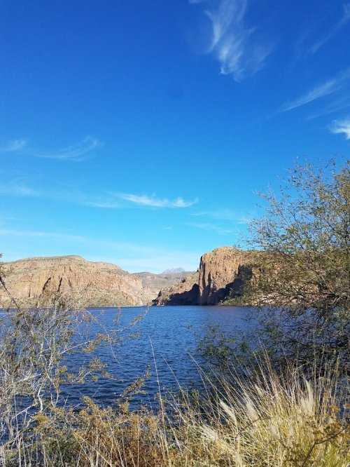 A serene lake surrounded by rocky cliffs and sparse vegetation under a clear blue sky.