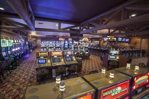 A spacious casino interior featuring rows of slot machines and a bar area, with dim lighting and a cozy atmosphere.