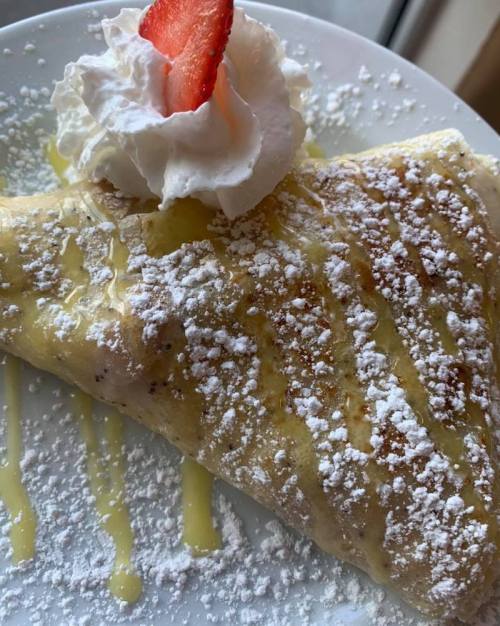 A delicious crepe topped with whipped cream, a strawberry, and drizzled with syrup and powdered sugar.