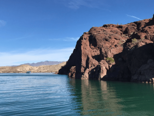 A serene lake surrounded by rocky cliffs and mountains under a clear blue sky.