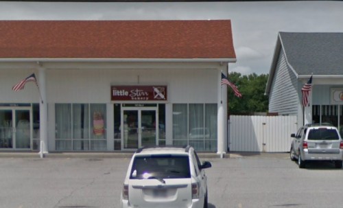 Exterior of a bakery named "little Stir" with American flags and parked cars in front.