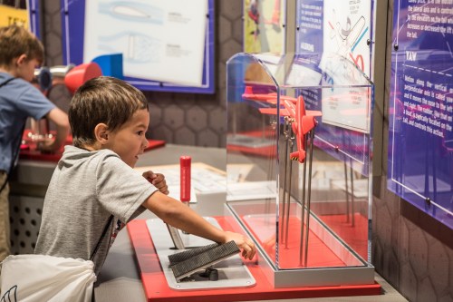 A young boy interacts with a hands-on exhibit, using a tool to explore a science display.